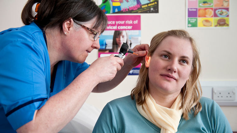 A female NHS member of staff inspects a female patient's ear with a torch